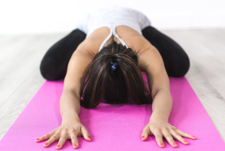 Woman lying in Child's Pose on pink yoga mat